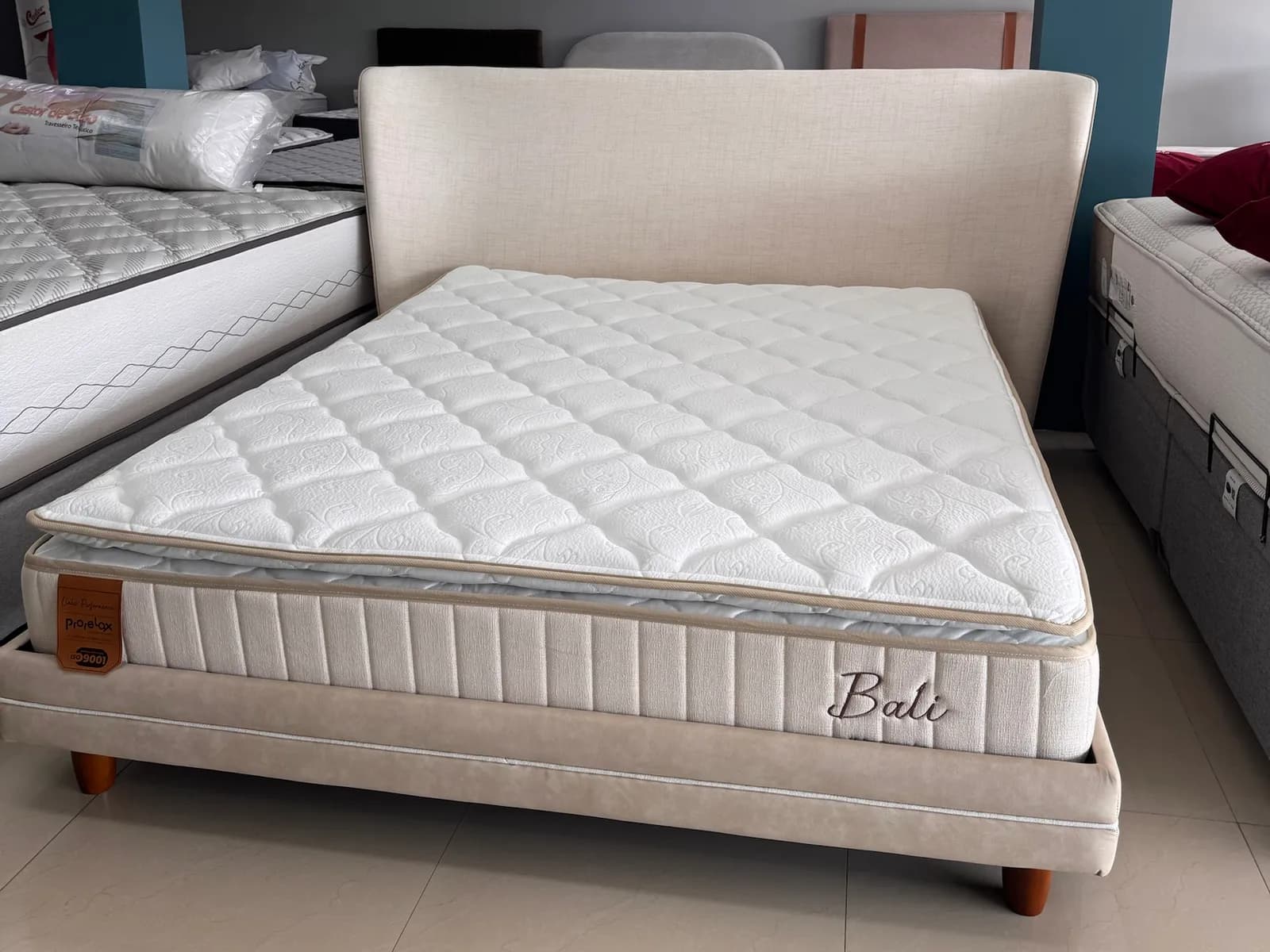 Colchão Prorelax Bali Turn Free com pillow top em cama estofada bege com cabeceira no showroom da Decorelar Colchões, em Inoã, Maricá