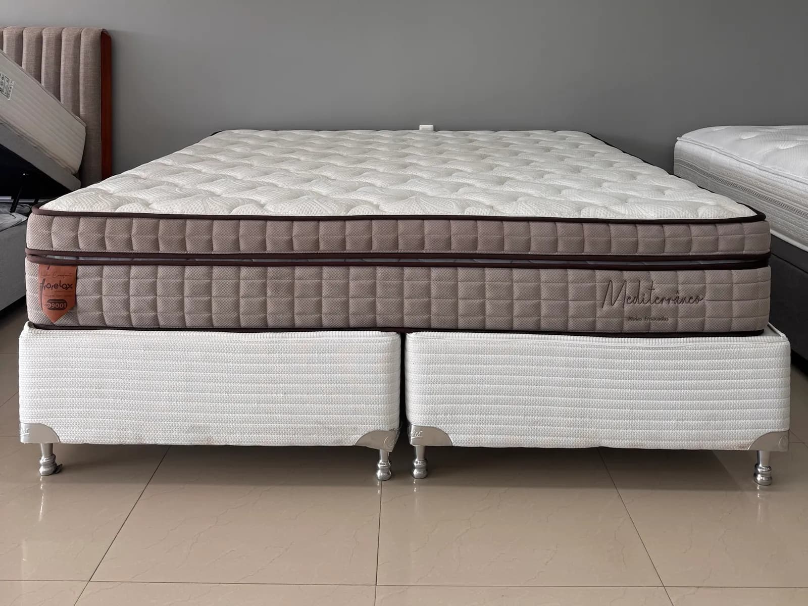 Colchão Prorelax Mediterrâneo com euro pillow e faixa cappuccino sobre box branco bipartido no showroom da Decorelar Colchões, em Inoã, Maricá