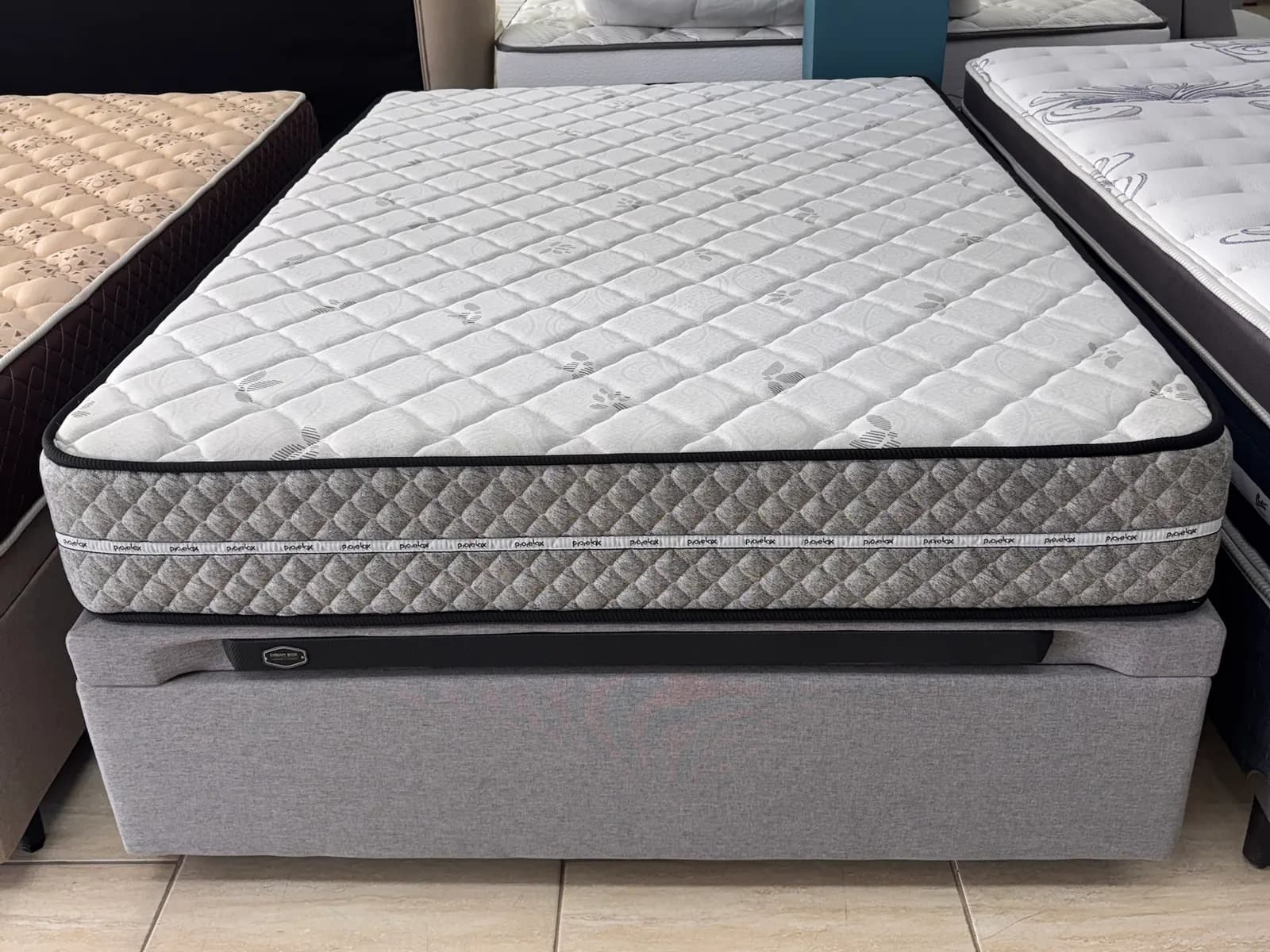 Colchão Prorelax Opala Max Firm com faixa lateral cinza sobre box baú cinza no showroom da Decorelar Colchões, em Inoã, Maricá